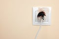 Burnt plug in power socket on beige wall, space for text. Electrical short circuit Royalty Free Stock Photo