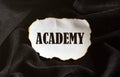 Burnt white piece of paper with text ACADEMY on a black fabric background Royalty Free Stock Photo