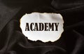 Burnt white piece of paper with text ACADEMY on a black fabric background