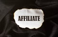 Burnt white piece of paper with text AFFILIATE on a black fabric background