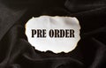 Burnt white piece of paper with text Pre Order on a black fabric background