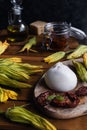 Burrata cheese, dried tomatoes, zucchini flowers, olive oil on rustic wooden table