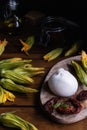 Burrata cheese, dried tomatoes, zucchini flowers, olive oil on rustic wooden table