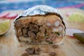 Burrito cut in half wrapped in foil surrounded by peppers, radishes, and lime