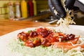 Burrito making process. To the meat, the chef adds cheese to beans and corn in tomato sauce, greens and tomatoes on pita