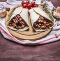 Burrito with meat and vegetables on a cutting board with tomatoes and garlic wooden rustic background close up