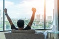 Business achievement concept with happy businessman relaxing in home office or hotel room, resting and raising fists with ambition