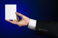 Business and advertising topic: Man in black suit holding a white blank card in his hand on a dark blue background in studio Royalty Free Stock Photo