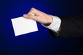 Business and advertising topic: Man in black suit holding a white blank card in his hand on a dark blue background in studio Royalty Free Stock Photo