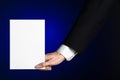 Business and advertising topic: Man in black suit holding a white blank card in his hand on a dark blue background in studio Royalty Free Stock Photo