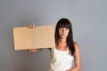 Business and advertising. A young brunette with a piercing, holding in one hand a cardboard for text. Gray background. Copy space