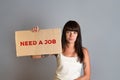 Business and advertising. A young brunette with a piercing, holding in one hand a cardboard with text NEED A JOB. Gray background Royalty Free Stock Photo