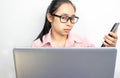 Business Asian young woman holding mobile phone while eyes looking at laptop. Using multiple devices on a desk at home Royalty Free Stock Photo