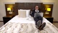 Business bald man with glasses and a stylish business suit, lying on the bed in the hotel room and looking at the laptop