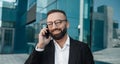 Business call. Confident bearded businessman chatting on cellphone standing outdoor in city Royalty Free Stock Photo