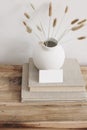 Business card mockup on vintage wooden table. Modern ceramic vase with dry Lagurus ovatus grass and pile of books. White