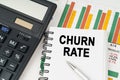 On business charts there is a calculator, a pen and a notepad with the inscription - CHURN RATE Royalty Free Stock Photo