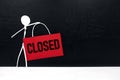 Business closure and bankruptcy concept. Stick man figure holding red we`re closed signage in black background with copy space. Royalty Free Stock Photo