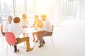 Business colleagues discussing while sitting at table by window in new office with yellow lens flare in background Royalty Free Stock Photo