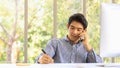 Business and Comminication Concept. Asian young businessman make a phone call by smartphone and take a note on paper in office Royalty Free Stock Photo