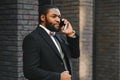 Business communications. Happy young African man in formal wear talking on the mobile phone and smiling while standing outdoors Royalty Free Stock Photo