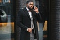 Business communications. Happy young African man in formal wear talking on the mobile phone and smiling while standing outdoors Royalty Free Stock Photo