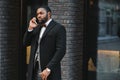 Business communications. Happy young African man in formal wear talking on the mobile phone and smiling while standing outdoors Royalty Free Stock Photo