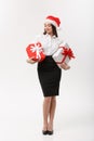 Business Concept - Beautiful young caucasian business woman with santa hat holding gift boxes with copy space on side. Royalty Free Stock Photo