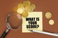 On a brown surface are coins, a pen, a magnifying glass and stickers with the inscription - WHAT IS YOUR SCORE