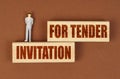 On wooden blocks with the inscription - INVITATION FOR TENDER, there is a miniature figure of a businessman.