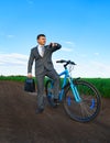 Business concept - A businessman rides a bicycle on a green grass field, he looks at his watch, dressed in a business suit, he has Royalty Free Stock Photo