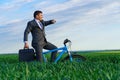 Business concept - A businessman rides a bicycle on a green grass field, he looks at his watch, dressed in a business suit, he has Royalty Free Stock Photo