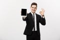Business Concept: Cheerful businessman in smart suit with pc tablet showing ok. over grey background. Royalty Free Stock Photo