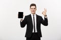 Business Concept: Cheerful businessman in smart suit with pc tablet showing ok. over grey background. Royalty Free Stock Photo