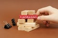 Clamps and wooden blocks lie on a brown surface, a person takes out a red block with the inscription - FUNDRAISING