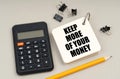 On a gray surface, a calculator, a pencil and a notepad with the inscription - Keep More Of Your Money