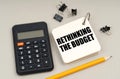 On a gray surface, a calculator, a pencil and a notepad with the inscription - Rethinking the budget