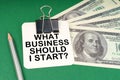 On a green surface, a pen, dollars and paper with the inscription - What Business Should I Start