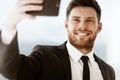 Business concept. Happy smiling young businessman at the office standing and making selfie or video chat conference