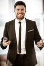 Business concept. Happy smiling young businessman standing in office holding a cell phone getting good news about his Royalty Free Stock Photo