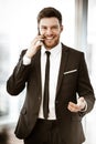 Business concept. Happy smiling young businessman standing in office talking on a cell phone getting good news about his Royalty Free Stock Photo