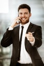 Business concept. Happy smiling young businessman standing in office talking on a cell phone getting good news about his Royalty Free Stock Photo