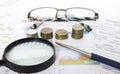 Business concept. Magnifying glass with coins, glasses and pen on finansial reports Royalty Free Stock Photo