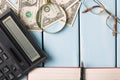 Business concept. Magnifying glass with glasses, dollar bills, notebook, fountain pen and calculator on blue wooden background