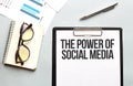 Business concept. Notebook with text THE POWER OF SOCIAL MEDIA sheet of white paper for notes, glasses in the white background Royalty Free Stock Photo