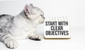 Business concept. Notebook with text START WITH CLEAR OBJECTIVES sheet of white paper and grey cat Royalty Free Stock Photo