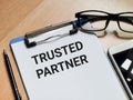 Phrase TRUSTED PARTNER written on paper clipboard with a pen,eye glasses and smartphone.