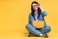 Business concept. Portrait of happy young woman in casual sitting on floor in lotus pose and holding laptop isolated over yellow Royalty Free Stock Photo