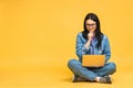 Business concept. Portrait of happy young woman in casual sitting on floor in lotus pose and holding laptop isolated over yellow Royalty Free Stock Photo