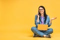 Business concept. Portrait of happy young woman in casual sitting on floor in lotus pose and holding laptop isolated over yellow Royalty Free Stock Photo